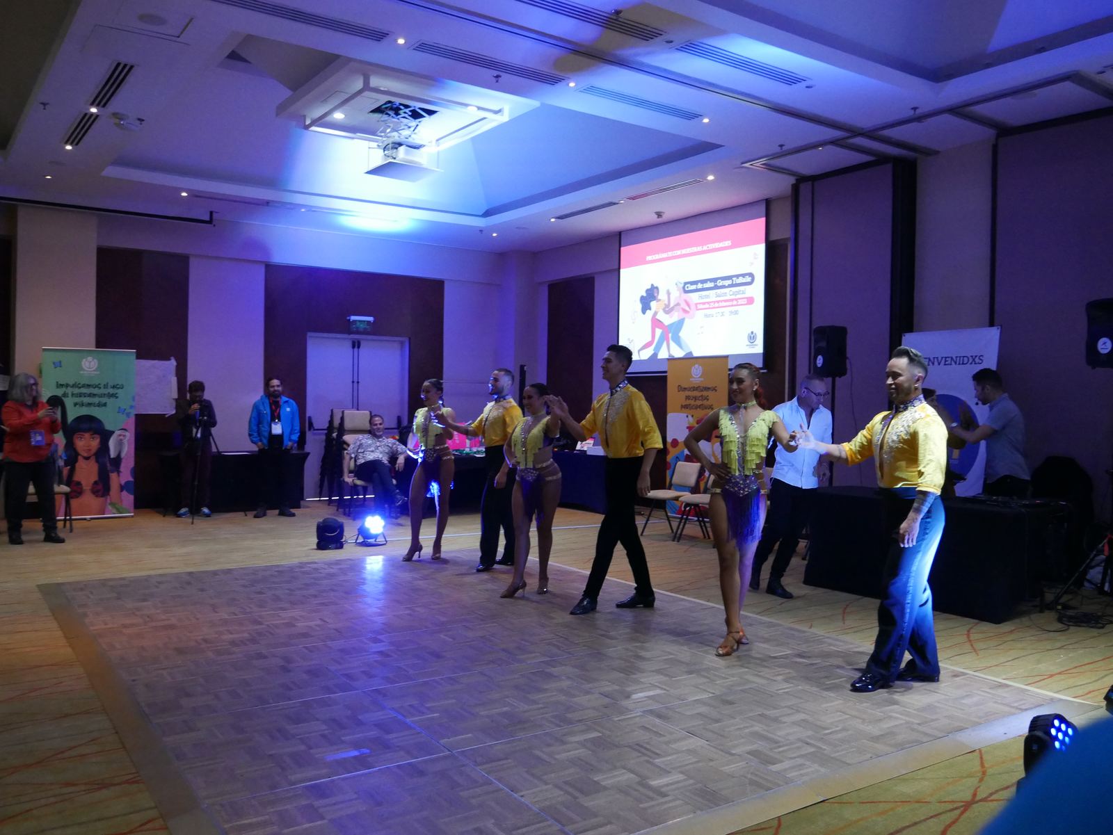 Couples practice salsa steps together in a conference hall dance class