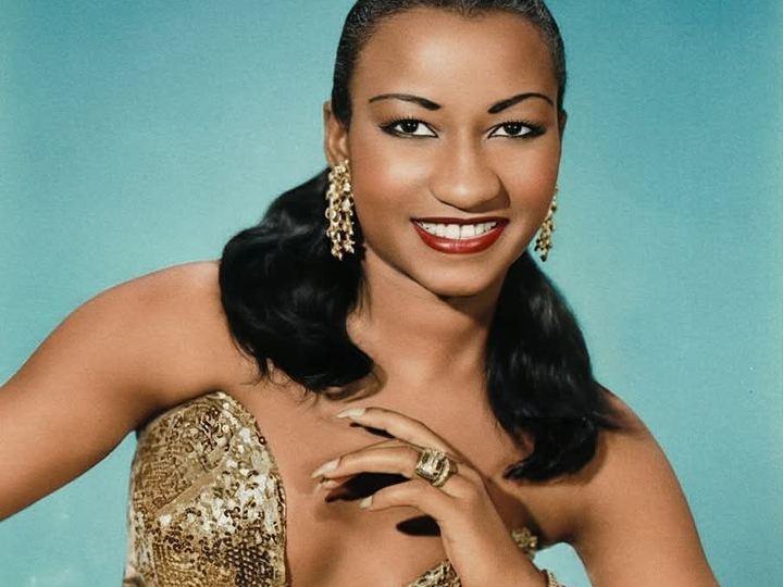 Color portrait of a smiling Celia Cruz in a gold sequined gown, 1957