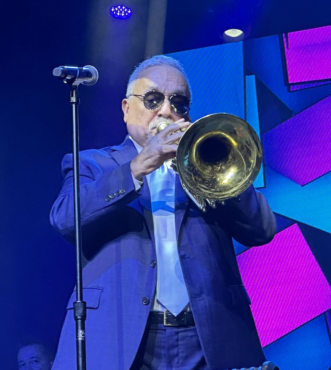 Willie Colón plays the trumpet on a stage lit in blue and purple